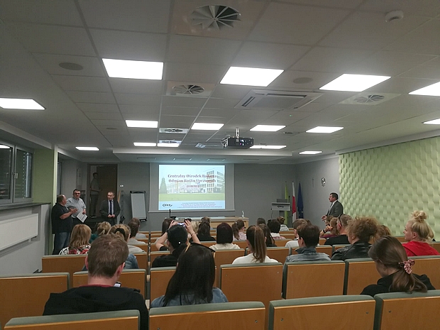 Zdjęcie 2 Wykłady w Centrali COBORU cz1 grupa ok 40 osób na sali wykładowej oraz wykładowcy COBORU i opiekunowie studentów. Na ekranie prezentacja z informacjami o COBORU